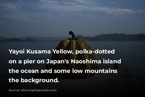 Yayoi Kusama Yellow, polka-dotted Pumpkin on a pier on Japan's Naoshima island with the ocean and some low mountains in the background.