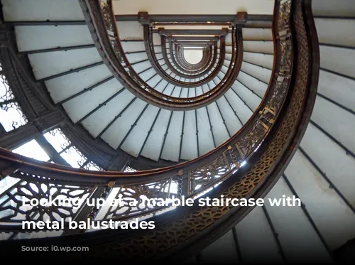 Looking up at a marble staircase with ornate metal balustrades