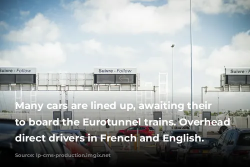 Many cars are lined up, awaiting their turn to board the Eurotunnel trains. Overhead signs direct drivers in French and English.