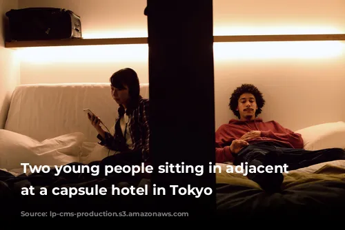 Two young people sitting in adjacent pods at a capsule hotel in Tokyo