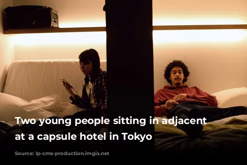 Two young people sitting in adjacent pods at a capsule hotel in Tokyo