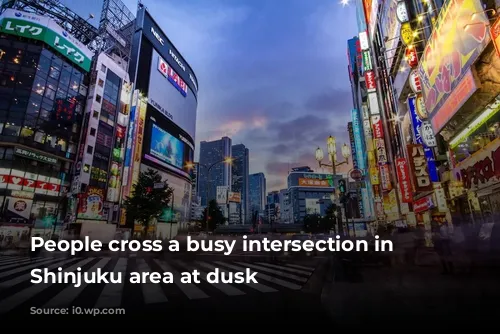 People cross a busy intersection in Tokyo's Shinjuku area at dusk