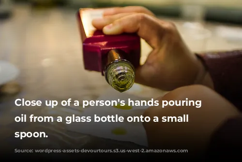 Close up of a person's hands pouring olive oil from a glass bottle onto a small white spoon.